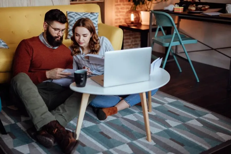 Young couple discussing investment options while sitting on the floor in the living room next to a coffee table with a laptop